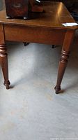 Close-up photo showing one turned leg of the wooden desk and part of the top surface in a basement setting.