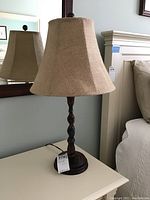 Lamp with twisted dark wood base and burlap shade on a light colored table in front of a mirror