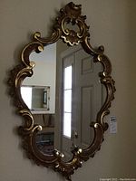 Full view of the vintage ornate wall mirror showing gilded carved frame and mirror surface reflecting a door.
