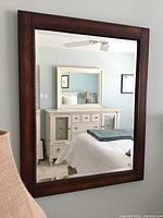 Full view of the mirror reflecting part of a room with dresser and bed.