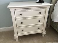 Front view of one nightstand showing three drawers, decorative molding, and metal knob pulls