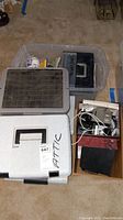 Clear and white filing boxes, black Olympus camera, and box with cables and electronic accessories.