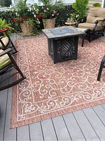 Full view of outdoor rug placed on deck with patio furniture and planters around.