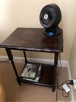 Wooden side table with a small black fan on top and books/photos on the lower shelf.