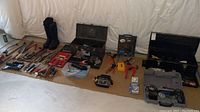 Wide shot showing two black rubber boots, various hand tools, garden tools, and toolboxes arranged on a floor mat.