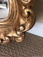Close-up photo of ornate gold frame showing detailed scrollwork and some wear.