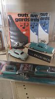 Photo showing three sets of Auto Gards in blister packaging, two vintage model cars - one light green and one teal in a box marked The 1964 Fords.