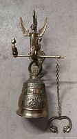 Full view of brass monastery bell showing angel figure, pull chain with heart handle, embossed designs, and overall shape.
