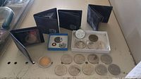 Coins laid out on surface showing nine 1975 Canadian single dollar coins and assorted commemorative coins in cases.
