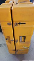 Side view of yellow plastic equipment case showing metal latches and handle with signs of wear and marks