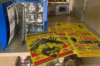Blue binder filled with pages of black and white vintage baseball card reproductions next to four reproduction fight posters laid out flat.