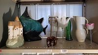 Shelf view showing all items including the green glass vase, wooden elephant, pottery fish, castle figurine, Crown Devon pitcher, and metal candle holder with glass bowl.