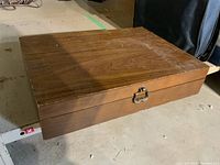 Closed wooden case with latch and wood grain finish containing the flatware set.