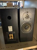 Front and rear views of two black wood veneer bookshelf speakers on shelf