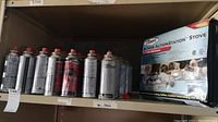Shelf with twenty-eight Sterno brand butane fuel cans and boxed Sterno Butane ActionStation Stove with original packaging visible.