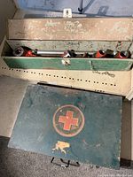 Green metal box with faded red cross emblem closed, containing the tool and die set.