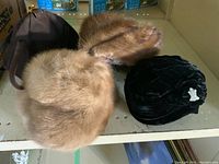 Brown mink hats and black velvet turban style hat with rhinestone pin shown together on a shelf.