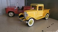 Yellow metal Buddy L pickup truck with whitewall tires and chrome detailing, shown from front angle, missing one headlight