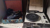 Photo showing the blue textured hard carrying case open with one black leather men's roller skate with wood wheels inside, and the Califone record player unit next to it with the operating instructions placed behind it.