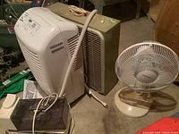 Whirlpool dehumidifier next to Airworks pedestal fan and box fan on concrete floor.