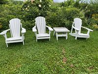 Three white Adirondack chairs arranged with matching side table on grass
