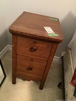 Full view of one oak wooden night table showing two drawers with round wooden knobs and a keyhole above each drawer, scratches visible on surface.