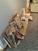 Overall view showing folded and framed tapestry canvases with floral designs, embroidery kits, and easel lined along the hallway.