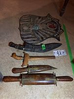 Five vintage weaponry pieces arranged on floor including daggers and decorative shield