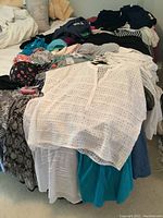 Full view of assorted women's tops and blouses in various colors and patterns laid out on a bed
