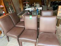 Six dark brown padded dining chairs arranged in a semicircle on a rug in a garage setting, showing front and side views.