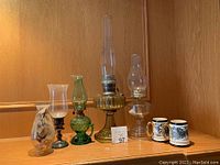 Wide shot showing all five antique lanterns and two ceramic mugs on a wooden shelf.