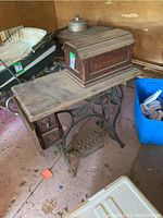 Photo of antique wooden sewing machine table with Raymond machine head cover on top, showing treadle base and drawers.