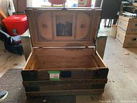 Open antique wooden trunk showing spacious interior with wear marks and dust. Painted artwork visible on inside of lid.