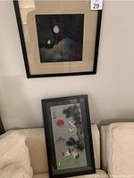 Both framed artworks, one on wall showing lotus flowers on black ground with gold leaf effect, other leaning showing cranes and red sun.