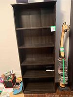 Front view of one dark wood bookshelf with three shelves visible, wall in background, and miscellaneous items alongside.