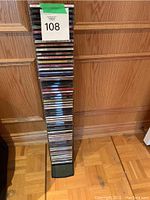 Full vertical stack of CDs on black stand against wood-paneled wall