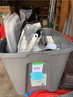 Top view of large Rubbermaid bin filled with various kitchen and baking equipment partially wrapped in bubble wrap and paper.