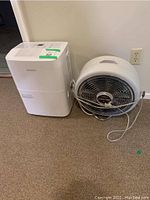 Photo shows one white Novair dehumidifier and one white round fan with power cord wrapped around it.