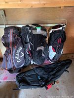 Photo showing four golf bags from various brands, including Callaway, arranged against a wall in a garage or storage area.