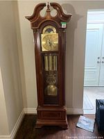 Full front view of wooden grandfather clock showing swan-neck pediment and base