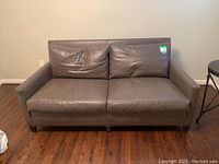 Front view of a gray leather sofa with two seat cushions and two back cushions on a hardwood floor.