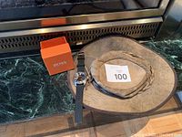 Photo showing a Hugo Boss wristwatch with black strap, orange box, and a brown leather hat with braided band.