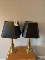 Two matching brass table lamps with black lampshades on a wooden surface against a beige wall