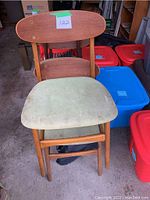 Front view of one teak chair showing wooden frame and worn light green upholstered seat with stains and discolorations.