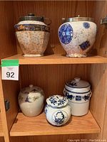 Full view of five oriental decorative jars on wood shelves.