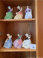 Six Royal Doulton porcelain figurines displayed on wooden shelves