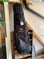 Black Wilson Staff wheeled sports bag hanging on a wall with stem and gardening tools nearby in a garage or shed setting.