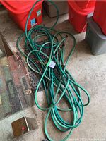 Photo of two green garden hoses coiled on the floor next to storage bins, showing one hose with a tapped fitting.