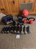 Photo of all gym equipment including dumbbells, kettlebells, medicine ball and grip trainers arranged on carpet in front of a wooden panel wall.