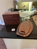 Wooden bread box closed with two wooden serving trays beside it on a kitchen counter.
